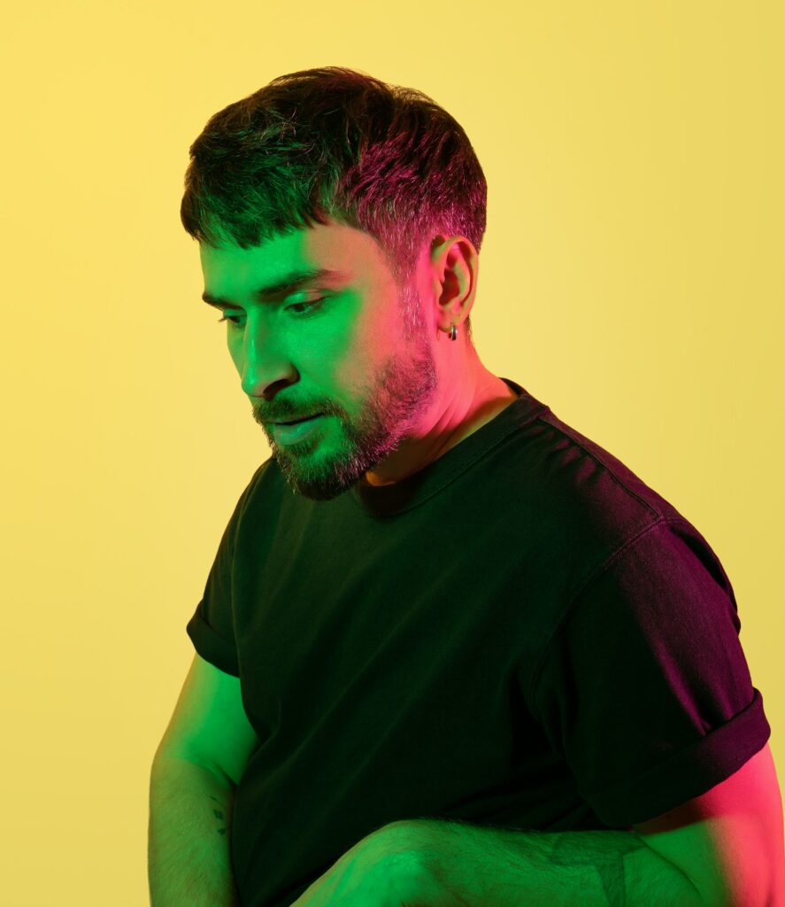 Artistic creative portrait. Pensive handsome man looking down in green, pink neon lights on yellow