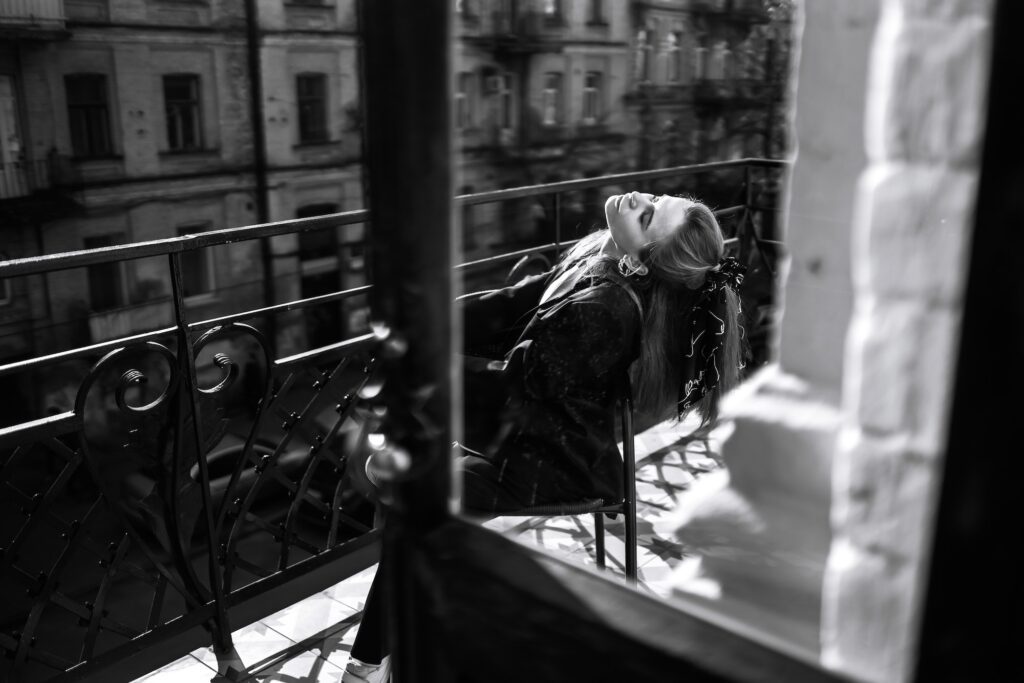 Black and white photo of stylish woman posing on balcony in city. Spring autumn fashion concept.